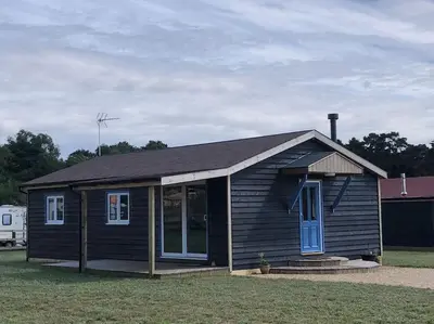 a small black house with blue doors and windows at Wagtail Lodge in Lackford