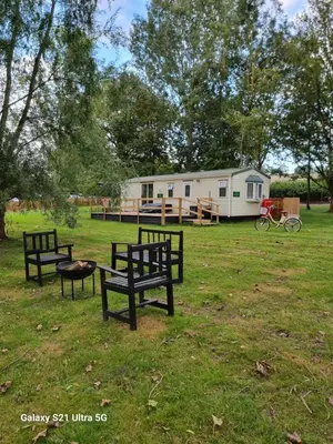 a group of benches in a field with a trailer at The Duck - Free Fishing, pets welcome - static caravan in Clare, Suffolk in Sudbury