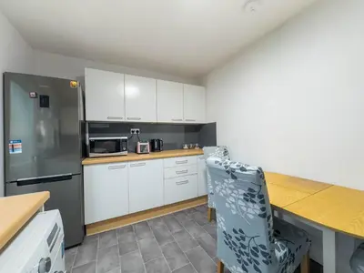 a kitchen with white cabinets and a table and a refrigerator at Southend Retreat KING SUITE Luxury stay with parking in Southend-on-Sea