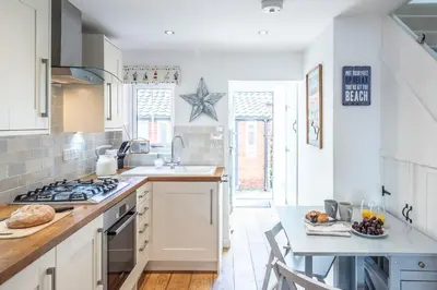 a kitchen with white cabinets and a table with a plate of food at Beachcomber, Aldeburgh in Aldeburgh