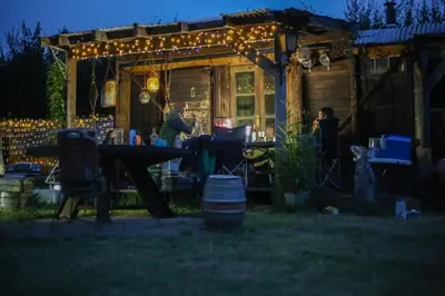 a woman sitting at a table in a backyard at night at Little Lodge Glamping in Halesworth