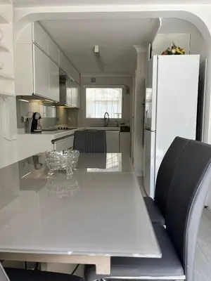 a white kitchen with a table and a refrigerator at Truehome Close to Stansted Airport in Harlow