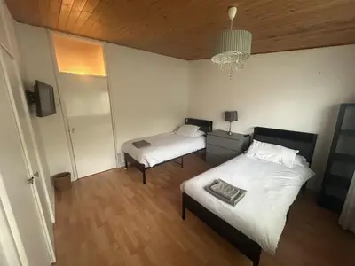a bedroom with two beds and a chandelier at Truehome Close to Stansted Airport in Harlow