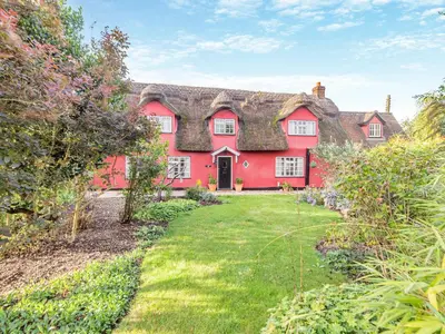 a red house with a thatched roof at All Saints Cottage in Saffron Walden