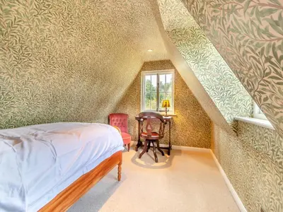 a bedroom with a bed and a chair and a window at All Saints Cottage in Saffron Walden