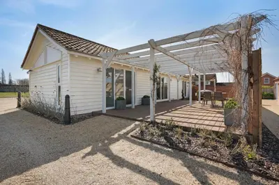 a white house with a pergola and a patio at Orchard Cottage in Saint Osyth