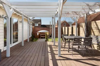 a white pergola on a deck with a table and chairs at Orchard Cottage in Saint Osyth