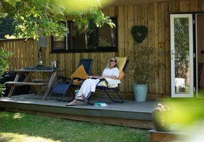 a woman sitting in chairs on the porch of a house at Copper Beech Lodge with Hot Tub, Games Room, Fire Pit in Toppesfield