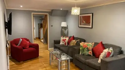 a living room with two couches and a red chair at Warm and Homely 4 Bed house w big Garden & Parking in Milton