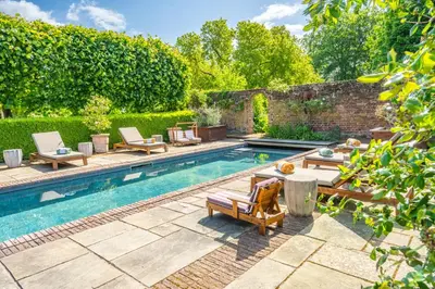 a swimming pool with lounge chairs and a table next to a brick wall at Spectacular thousand year old Medieval manor house - Flemings Hall in Ipswich