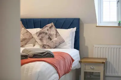 a bed with a blue headboard and pillows on it at Kestrel Gardens Five Bedroom Homes in Great Dunmow