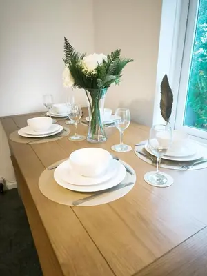 a wooden table with plates and glasses and a vase of flowers at Comfortable 2-Bed Home, Perfect for Work and Leisure in Colchester in Colchester