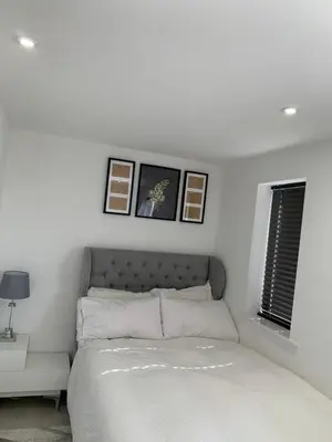 a white bedroom with a bed and pictures on the wall at BYK Homes, Hotels and Suites in Grays Thurrock