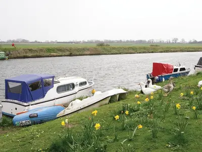 two boats are docked on the side of a river at Greenbank Cottage in Hilgay