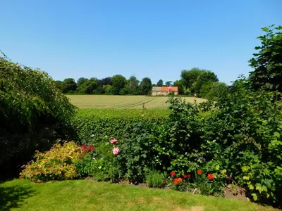 a garden with flowers and a field in the background at Greenbank Cottage in Hilgay