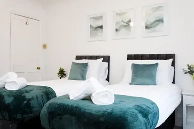 two beds with green ottomans in a bedroom at Cosy House - Stanstead Airport in Bishops Stortford