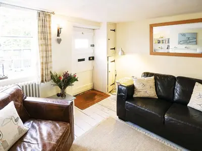 a living room with a leather couch and a window at 6 Town Steps by The Suffolk Cottage Collection in Aldeburgh