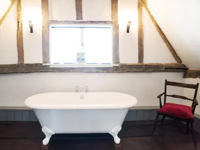 a white bath tub in a bathroom with a chair at The Cross Wing by The Suffolk Cottage Collection in Peasenhall