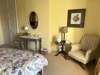 a bedroom with a bed and a chair and a table at Peacocks Tearoom and Fine B&B in Ely