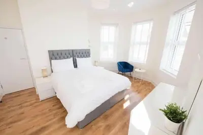 a white bedroom with a large bed and a blue chair at Seaview Apartments - 28-29 Marine Parade, Harwich - Perfect for business & long term stays in Dovercourt
