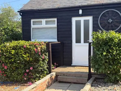 a black house with a white door and some bushes at Colne cabin in Earls Colne
