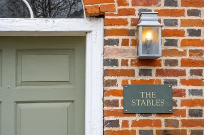 a sign on a brick building with a light next to a door at Belchamp Hall Stables in Belchamp Otten
