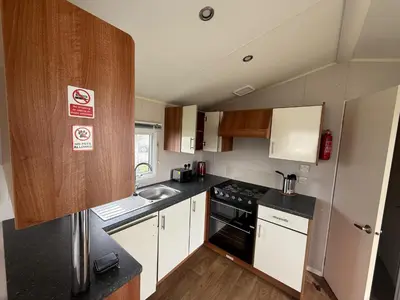 a small kitchen with a sink and a stove at 6 Beds 2 Sofa bed Family friendly - unlimited Wi-Fi, Warm, Cozy Sun decking Caravan at Seawick Holiday Park in Saint Osyth