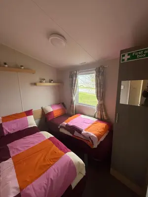 two beds in a small room with a window at 6 Beds 2 Sofa bed Family friendly - unlimited Wi-Fi, Warm, Cozy Sun decking Caravan at Seawick Holiday Park in Saint Osyth
