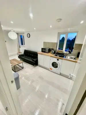 a living room with a black couch and a kitchen at cozy 1 bedroom flat near cambridge city centre in Milton