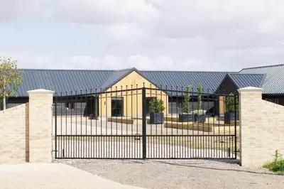 a fence in front of a house with a black roof at Beautiful 2 Bedroom Barn -Stansted Airport 2 miles in Elsenham