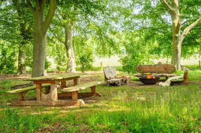a picnic table and bench in a park with trees at A Duke's Spectacular grand folly - The Temple in Euston