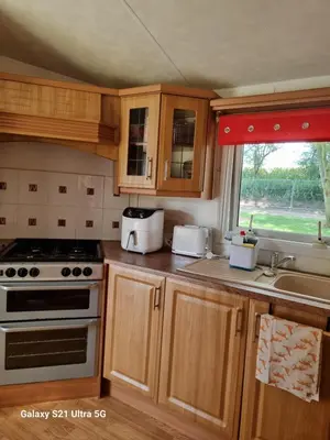 a kitchen with wooden cabinets and a stove top oven at The Fox - Free Fishing, pets welcome - static caravan in Clare, Suffolk in Clare