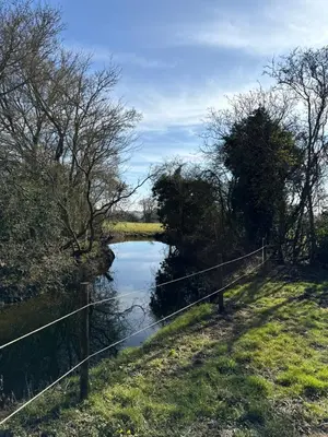 a fence next to a river with a bridge at 'Russet' Hut on fruit farm in Charsfield