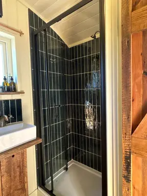 a bathroom with a shower with black tile at 'Russet' Hut on fruit farm in Charsfield