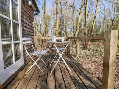 a table and chairs on a wooden deck with trees at Woodlands Retreat Shepherd's Hut in Woodbridge