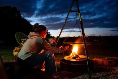 a woman sitting in front of a fire at Farm woodland riverview cabin bbq firepit pet friendly in Hertford