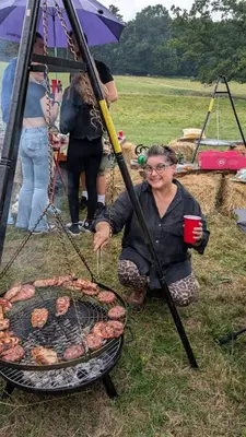 a woman is cooking food on a grill at Hertford belltent farm stay riverside firepit bbq in Hertford