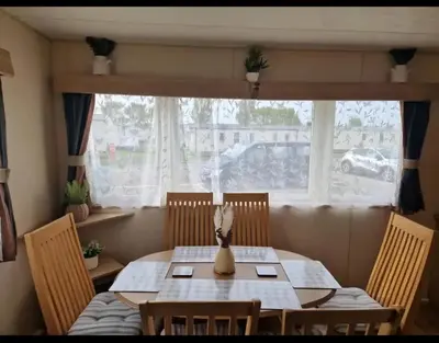 a dining room table with chairs and a window at House of Eminence Holidays in Saint Osyth