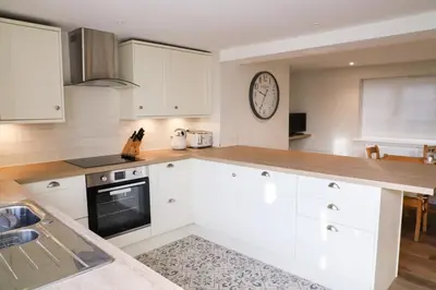 a kitchen with white cabinets and a clock on the wall at Beautifully refurbished 3 bedroom cottage in Ashdon