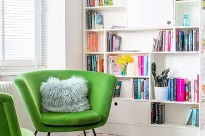 a green chair with a fuzzy pillow in front of a book shelf at Edinburgh House in Aldeburgh