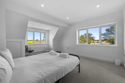 a white bedroom with a bed and two windows at Bakers Cottage, Blackmore End in Gosfield