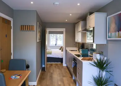 a kitchen with white cabinets and a table and a bed at Russet Suite - The Apple Barn in Pettistree