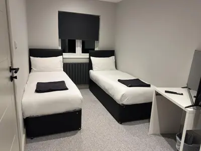 two beds in a small room with a desk at Abbey Rooms in Waltham Abbey
