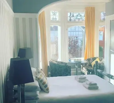 a bedroom with a bed and a table and windows at The Cobham Hotel in Southend-on-Sea