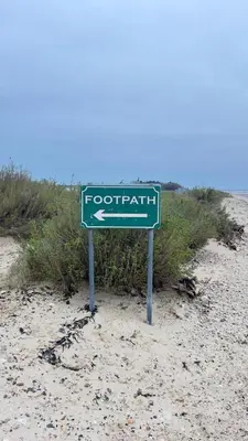 a green street sign on the sand on a beach at The Beach House East Mersea in Mersea Island