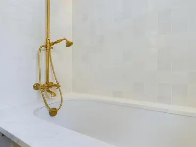 a bath tub with a gold shower in a bathroom at Stunning Heritage Cottage- The Heart of Old Leigh in Southend-on-Sea