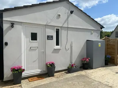 a small white shed with a door and flowers at The Annexe Long Melford in Long Melford