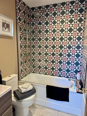 a bathroom with a tub and a toilet and a tile wall at Quaint Bury St Edmunds Cottage in Bury Saint Edmunds
