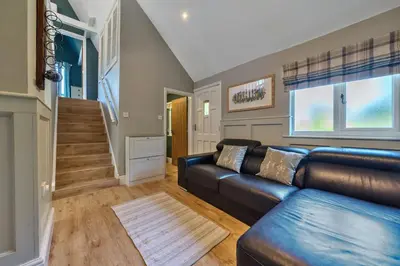 a living room with a leather couch and a staircase at The Folly, Thorpe Forest in Brettenham