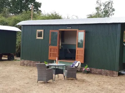 a green house with chairs and a table in front of it at Delightful shepherd's hut in a rural location in North Fambridge